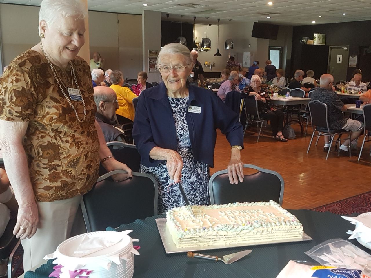 Dawn Skennerton cutting the cake while Janess Peterson looks on.